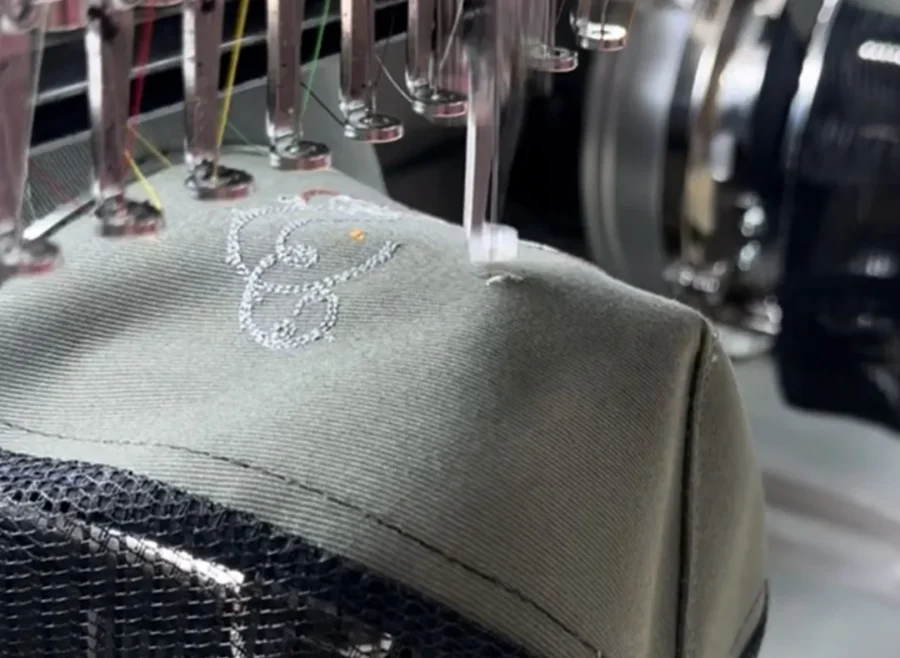 Machine à broder industrielle réalisant une broderie blanche sur une casquette textile personnalisée.